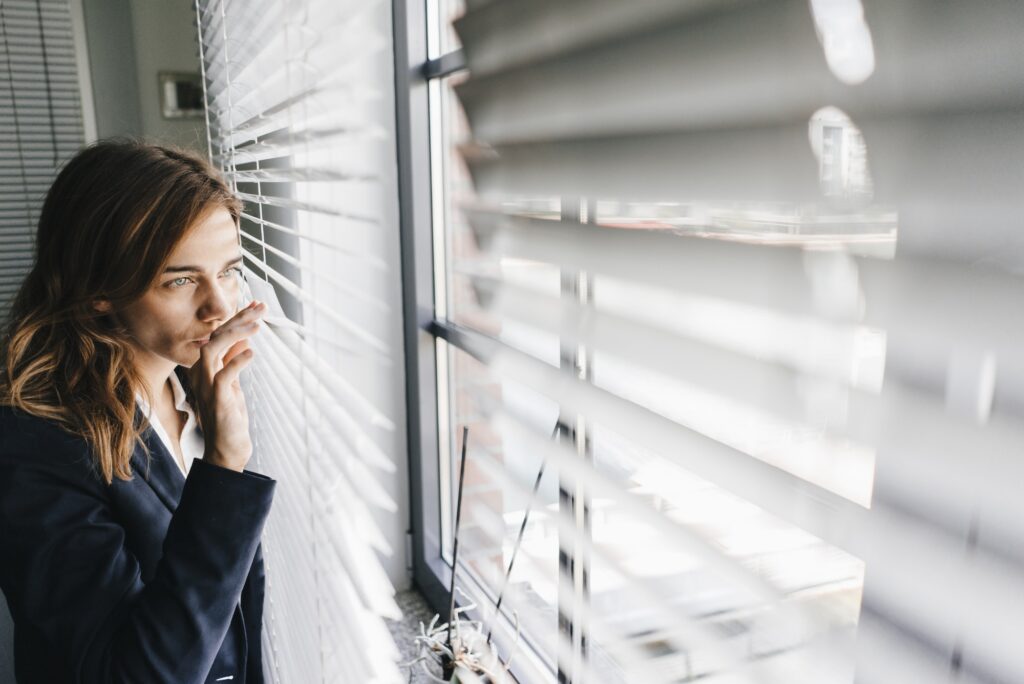 Woman standing by window, spying through blinds